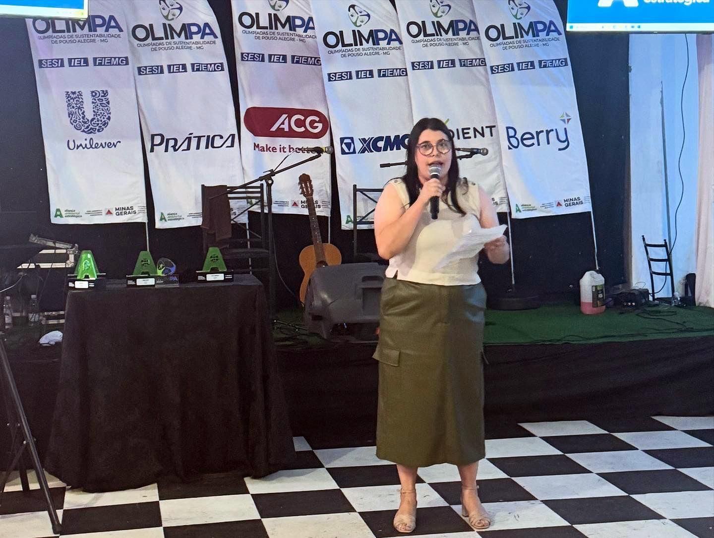 Uma mulher está de pé no palco segurando um microfone e um pedaço de papel.