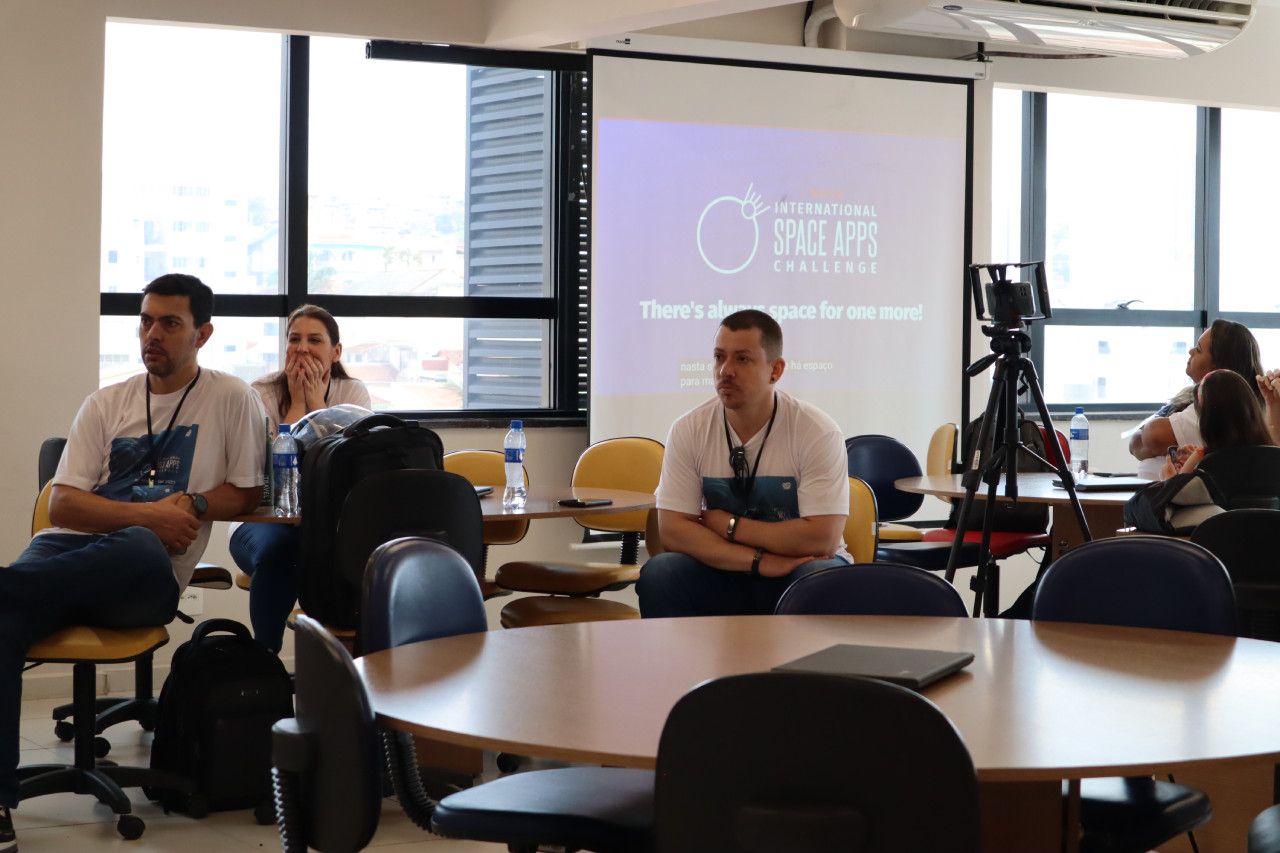 Um grupo de pessoas está sentado em mesas em frente a uma tela de projetor.