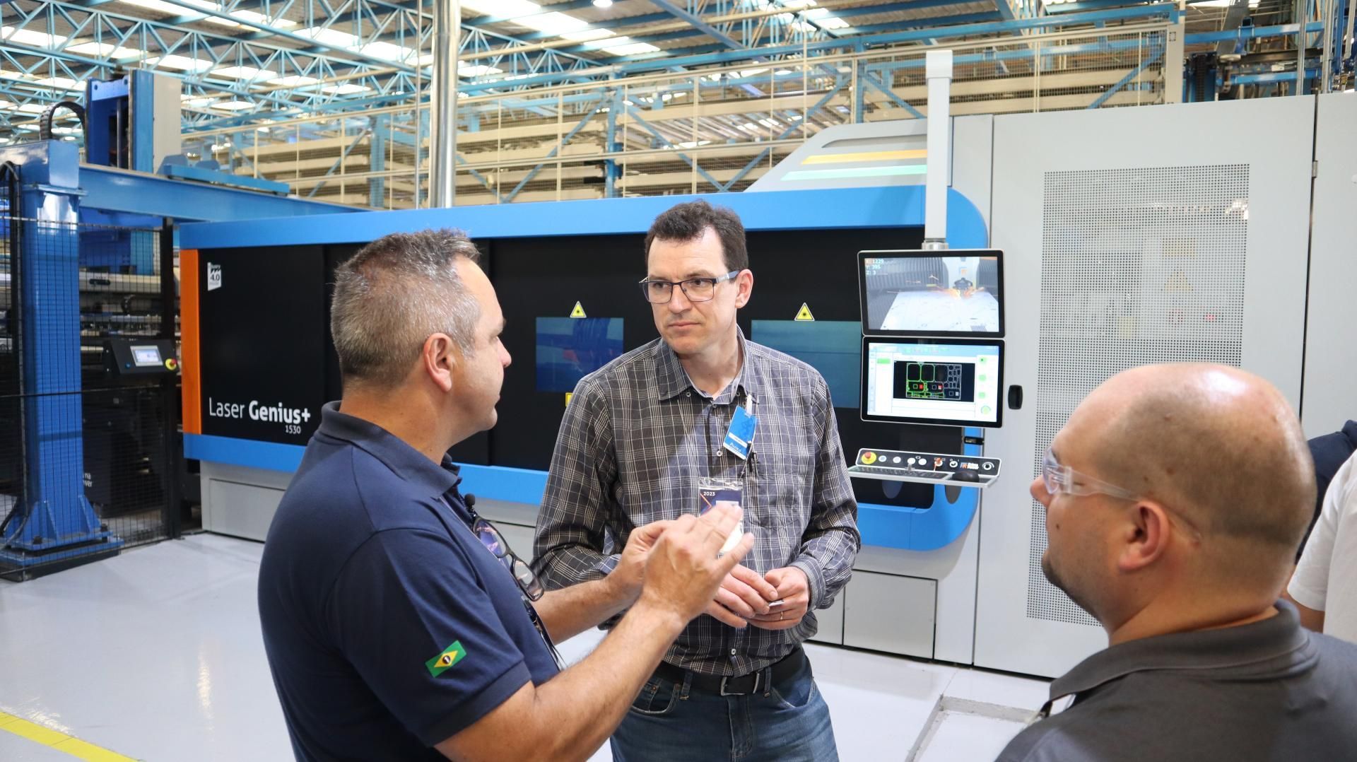 Um grupo de homens está em uma fábrica conversando entre si.