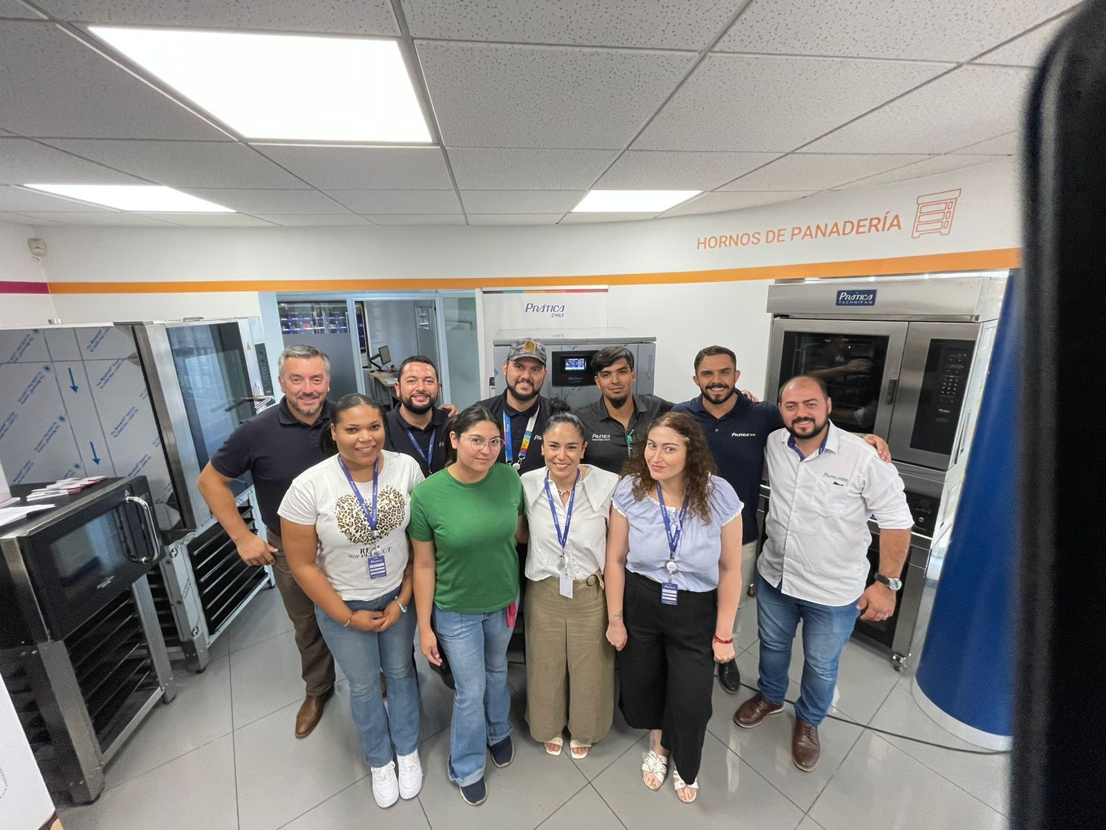 Grupo de pessoas em uma cozinha industrial, posando em frente a equipamentos comerciais, sorrindo.