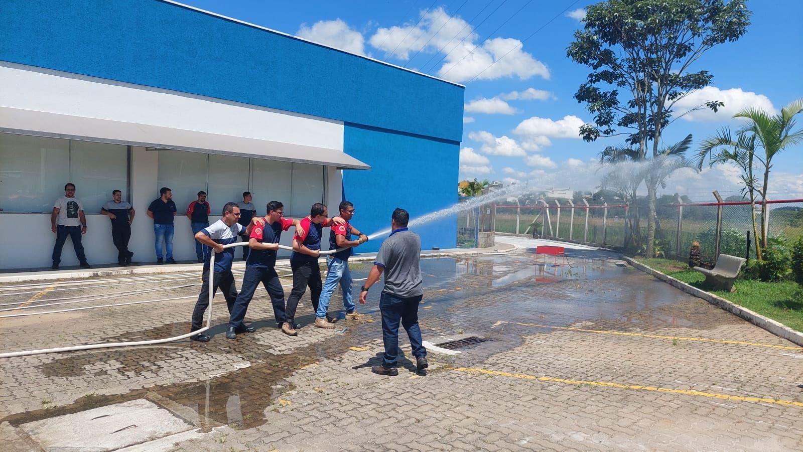 Um grupo de homens está jogando água de uma mangueira em frente a um prédio azul.