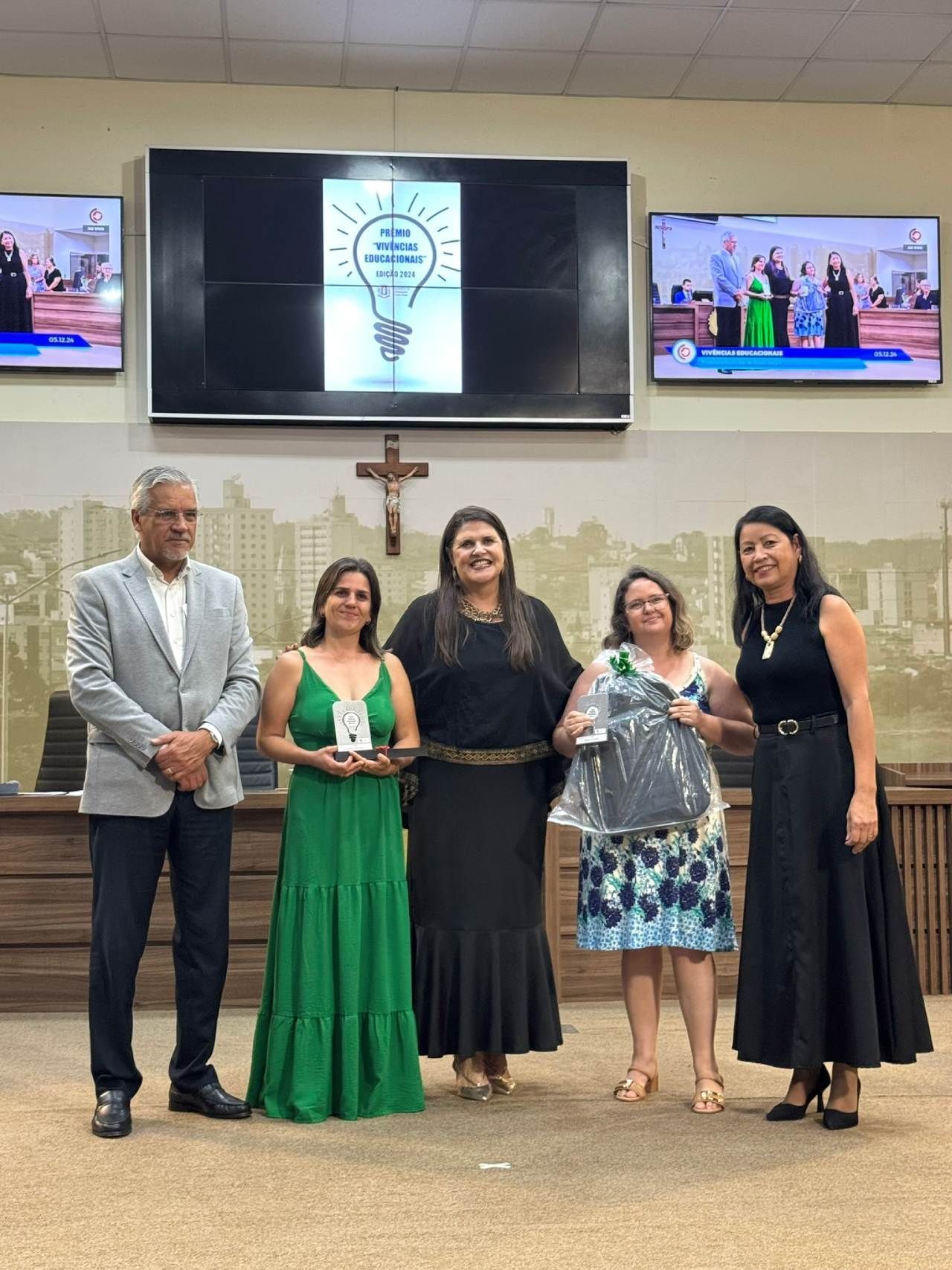 Um grupo de mulheres estão de pé, uma ao lado da outra, em frente a uma tela grande.