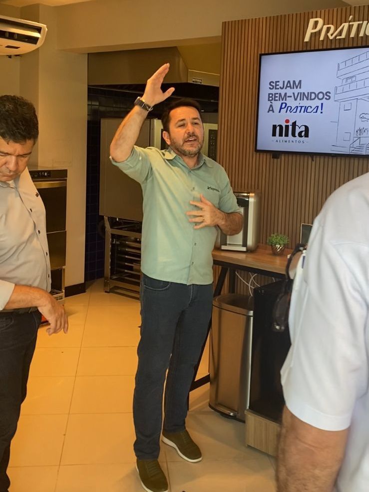 Um homem está parado em frente a uma televisão em uma cozinha.