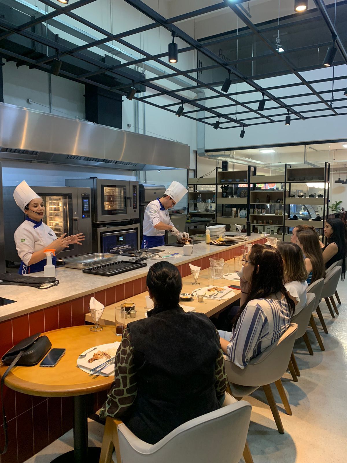 Um grupo de pessoas está sentado em mesas em um restaurante observando um chef preparando comida.