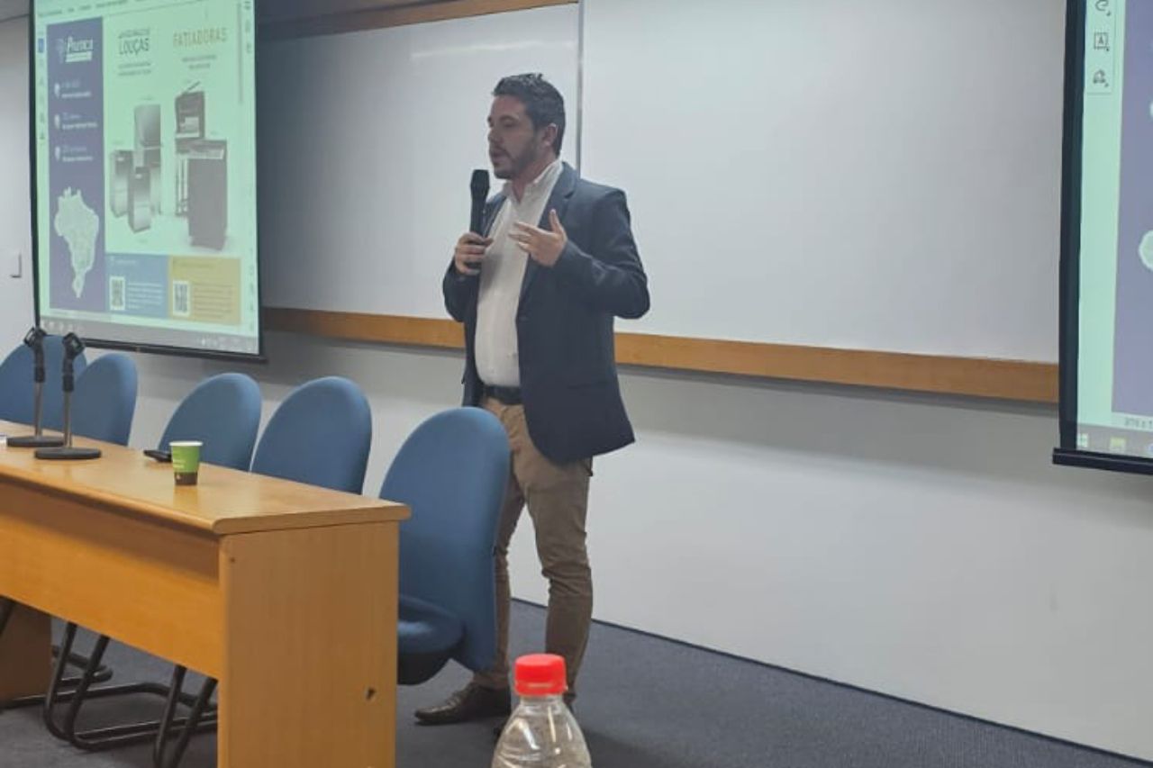 Um homem está fazendo uma apresentação em uma sala de aula enquanto segura um microfone.