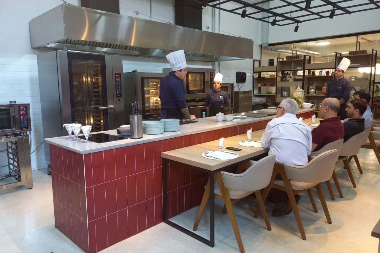 Um grupo de pessoas está sentado em mesas em uma cozinha.