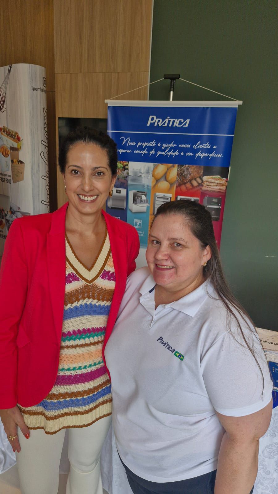 Duas mulheres estão posando para uma foto em frente a um banner.
