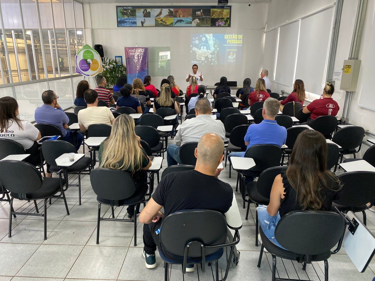 Um grupo de pessoas está sentado em uma sala de aula assistindo a uma apresentação.