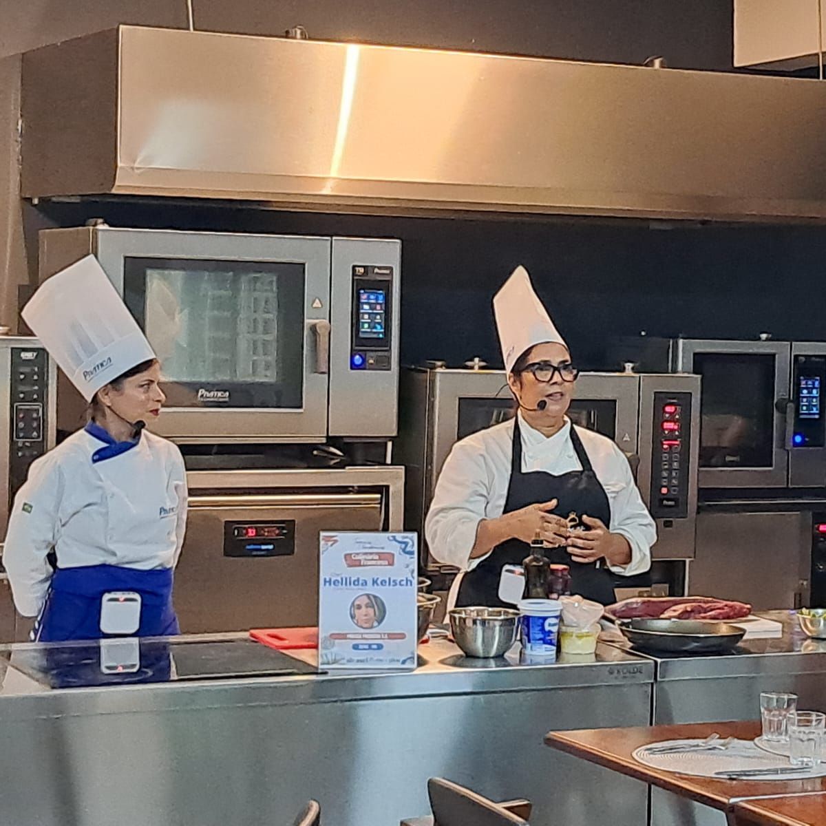 Dois chefs estão em uma cozinha conversando entre si.