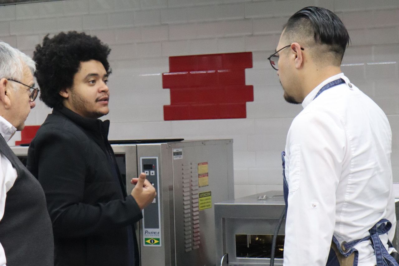 Um grupo de homens está em uma cozinha conversando entre si.