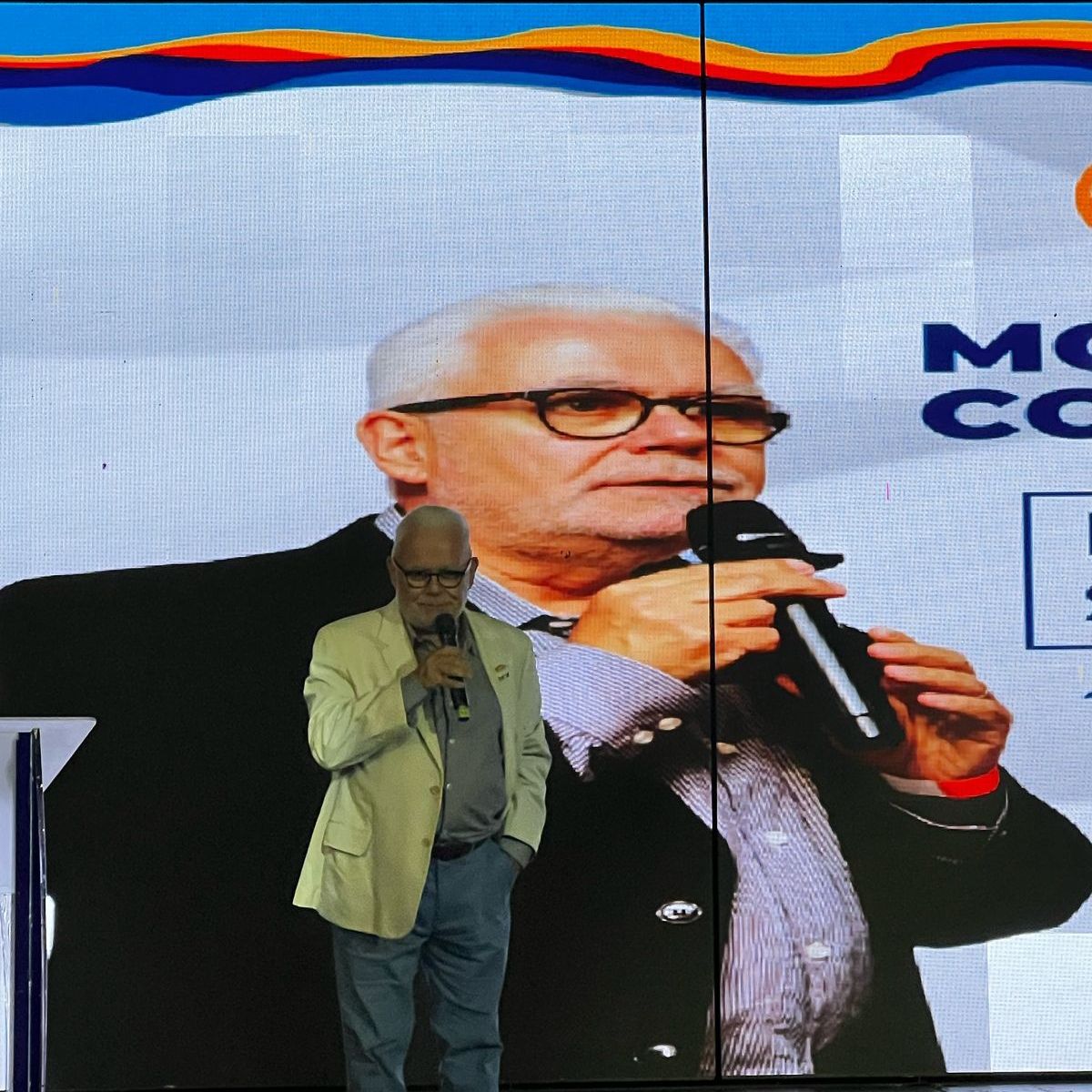 Um homem segurando um microfone em frente a uma placa que diz mc