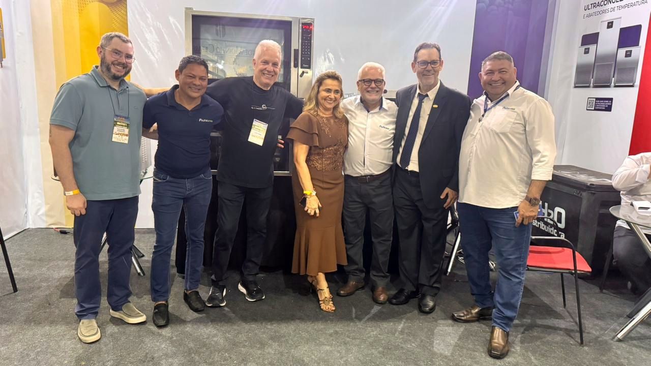 Grupo de sete pessoas posando juntas em um estande de feira, sorrindo para a câmera.