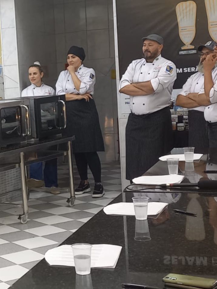 Um grupo de chefs estão em volta de uma mesa com copos de água