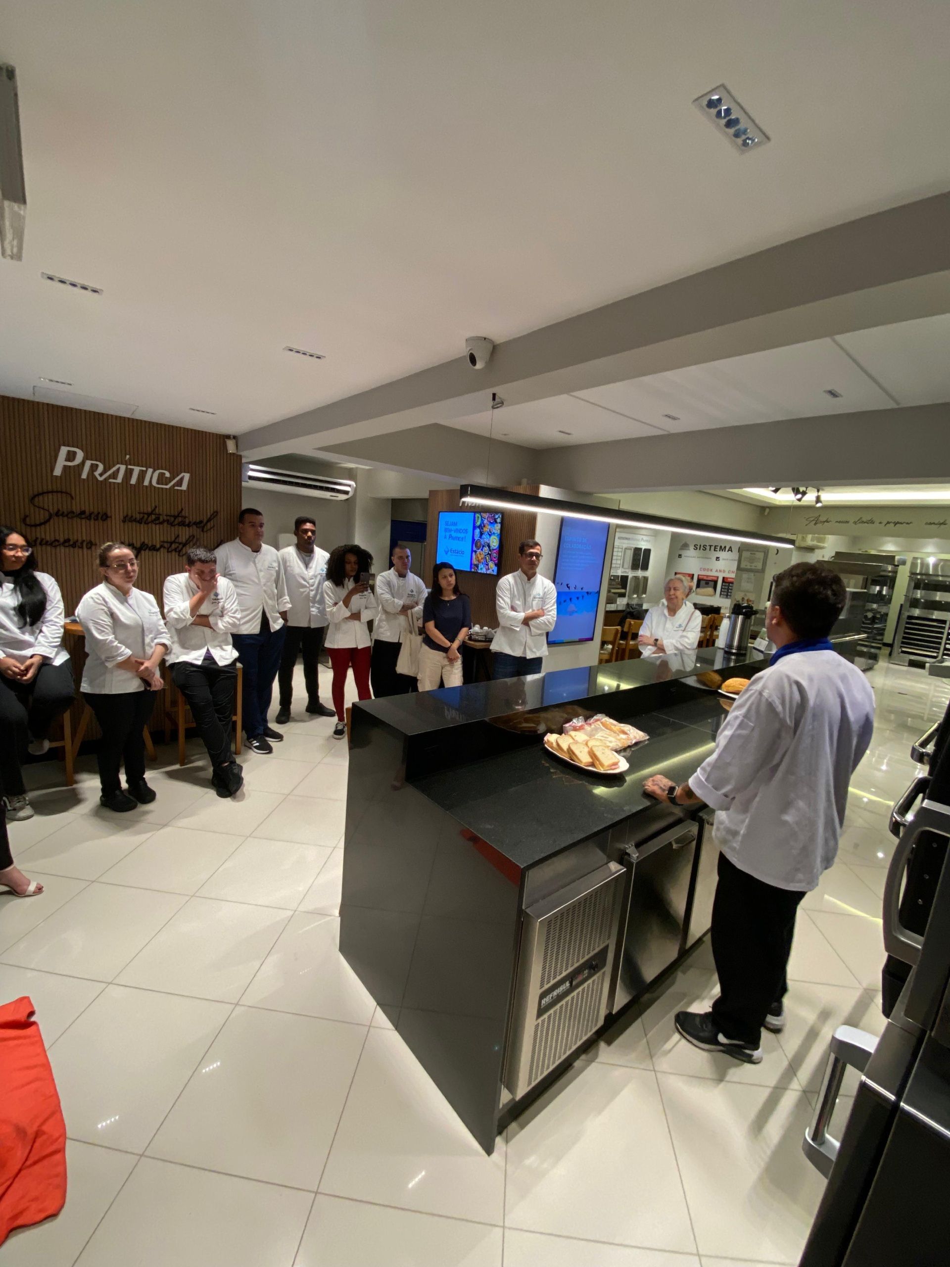 Um grupo de pessoas está em pé ao redor de um balcão em uma cozinha.