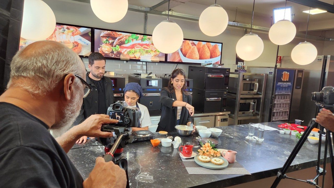 Um homem está tirando uma foto de uma mulher cozinhando em uma cozinha.