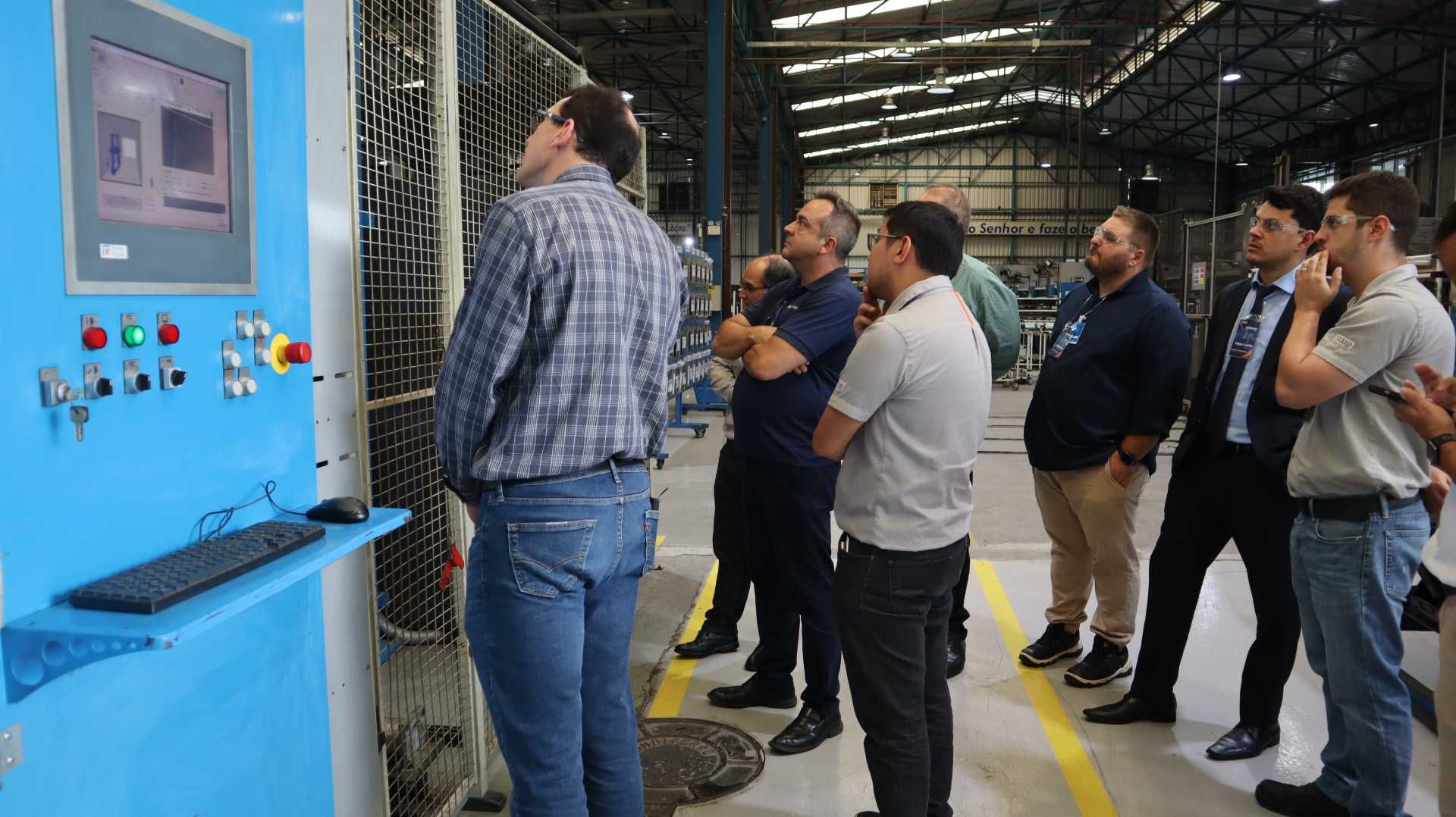 Um grupo de homens está em volta de uma máquina em uma fábrica.