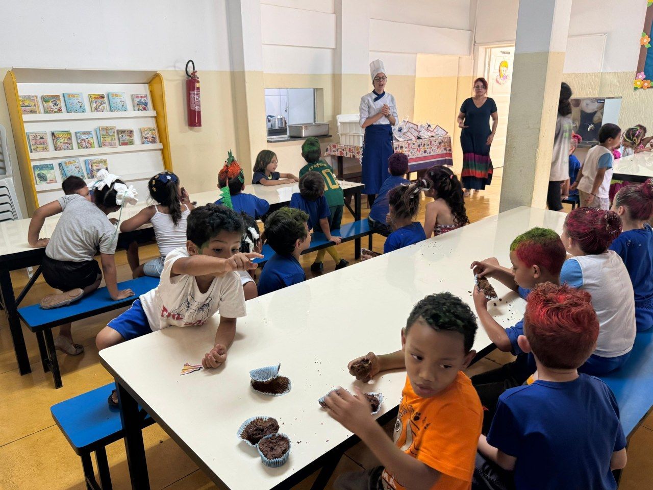 Um grupo de crianças está sentado em mesas compridas no refeitório de uma escola.