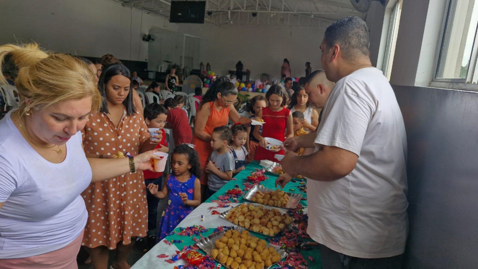 Um grupo de pessoas está em pé ao redor de uma mesa comendo.