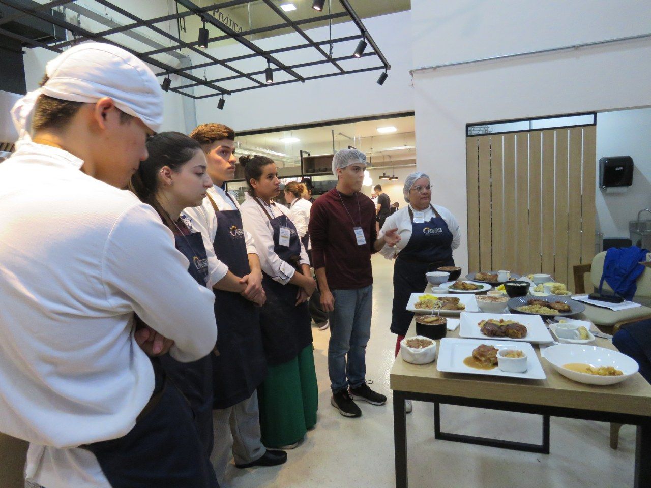 Um grupo de pessoas está de pé ao redor de uma mesa com pratos de comida sobre ela.