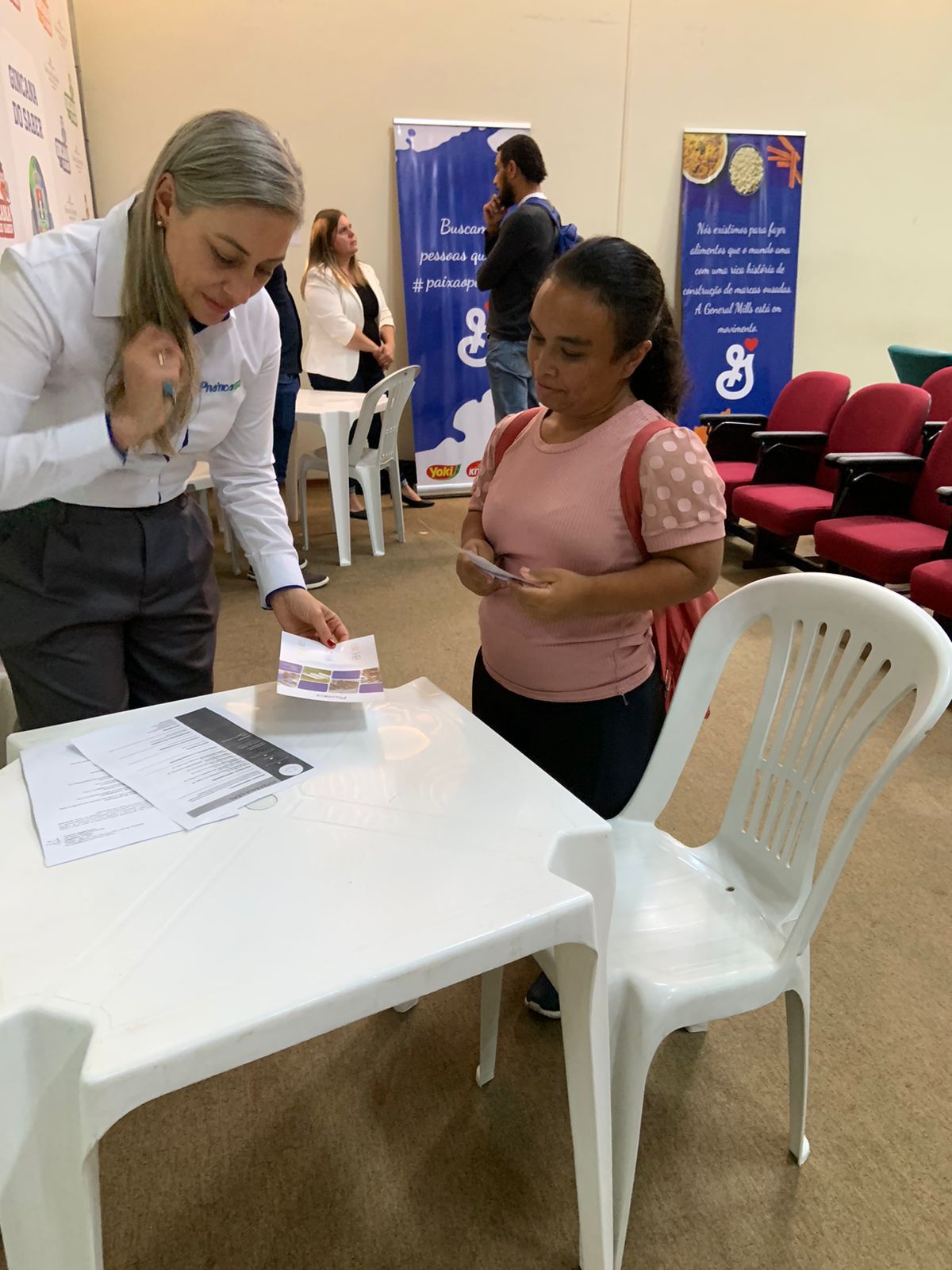 Uma mulher está de pé ao lado de uma mulher sentada à mesa.