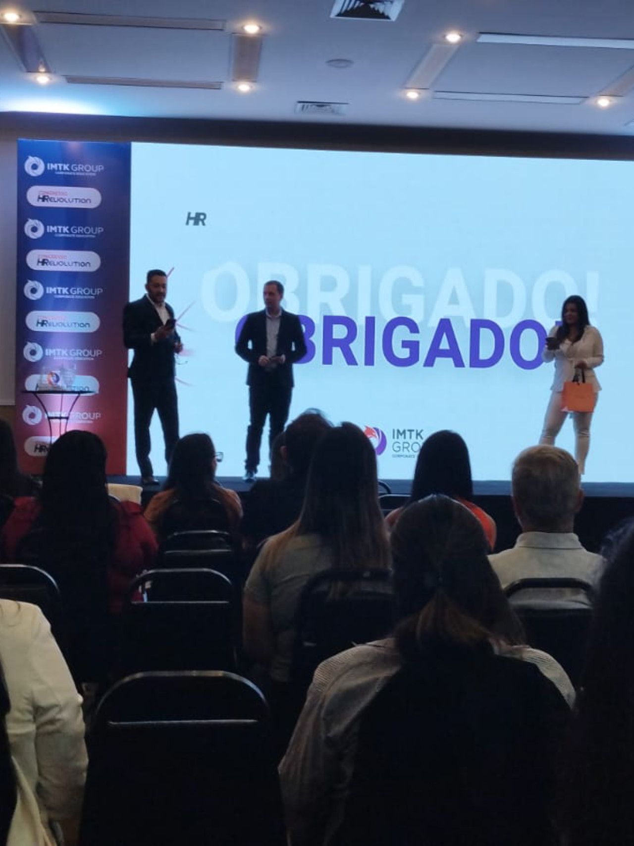 Um grupo de pessoas sentadas em frente a uma tela que diz obrigado