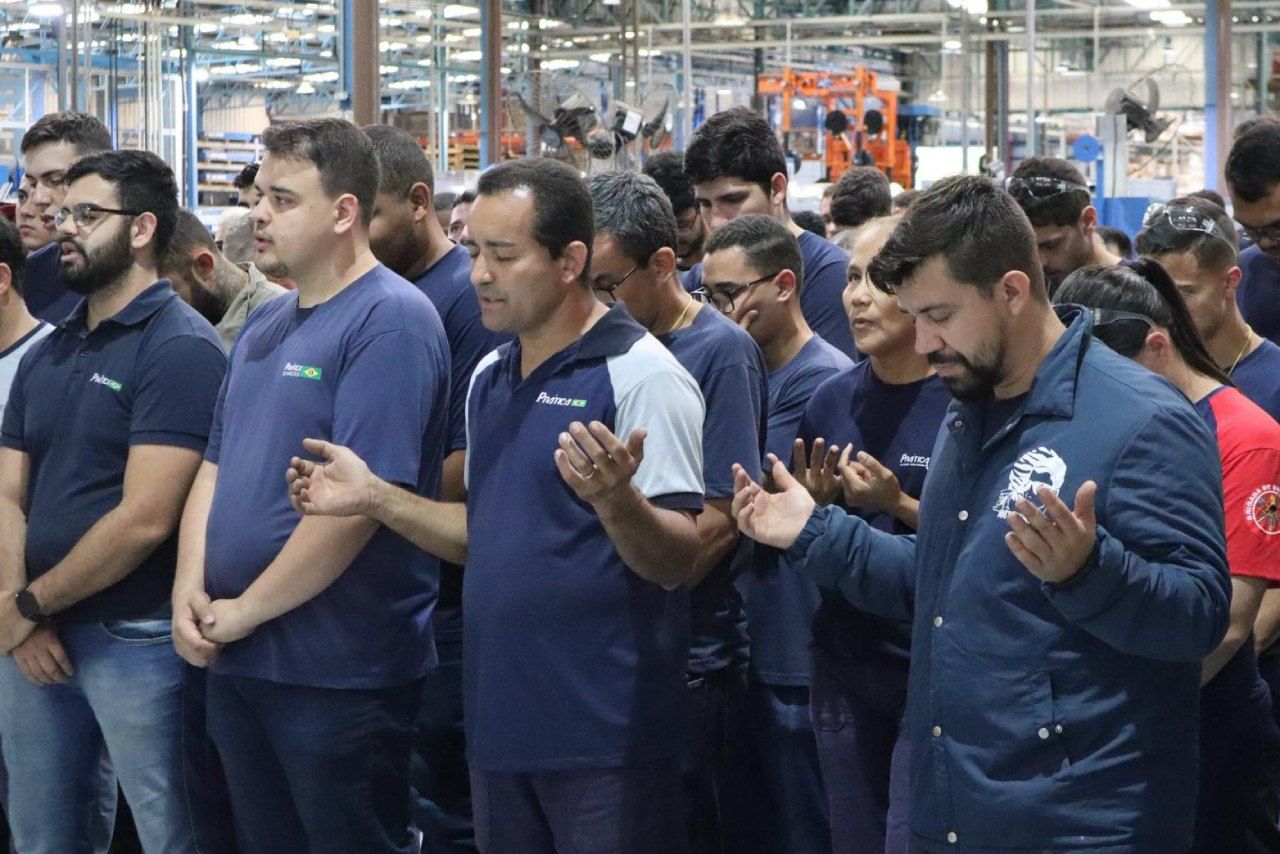 Um grupo de homens está rezando em uma fábrica.