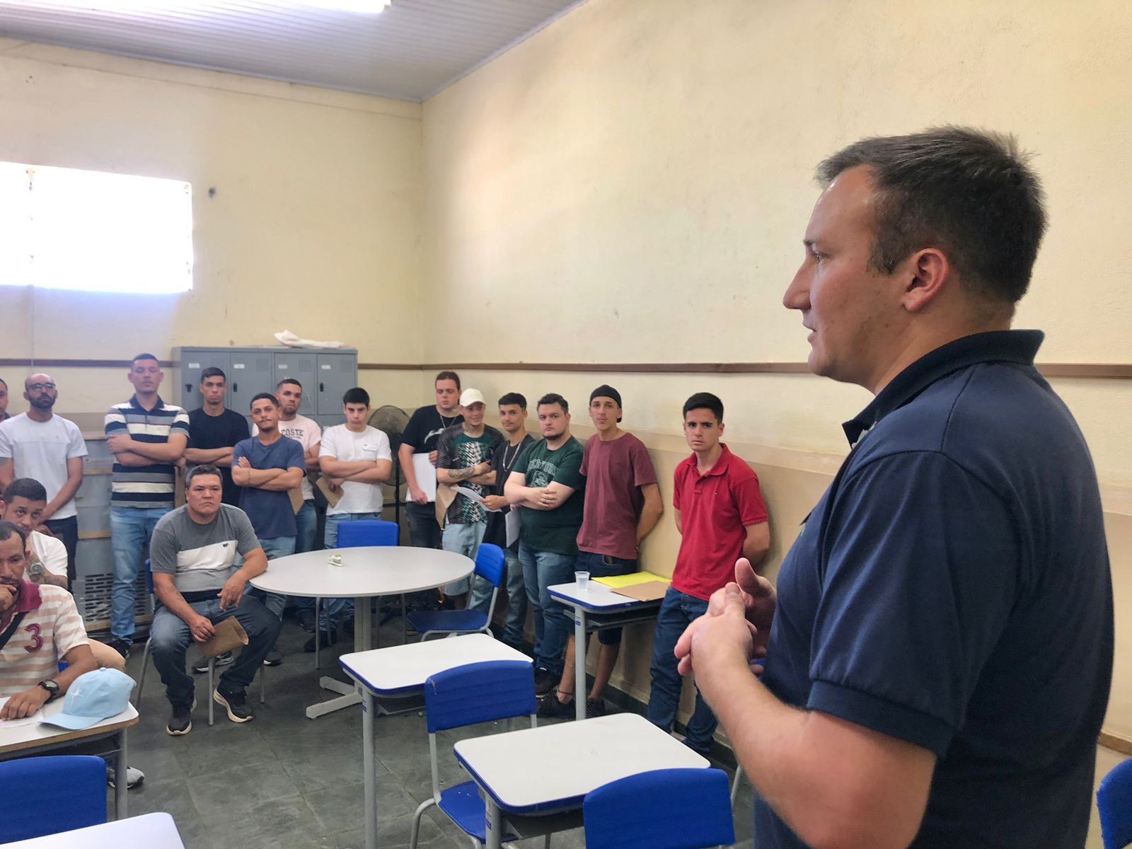 Um homem está parado na frente de um grupo de homens em uma sala de aula.