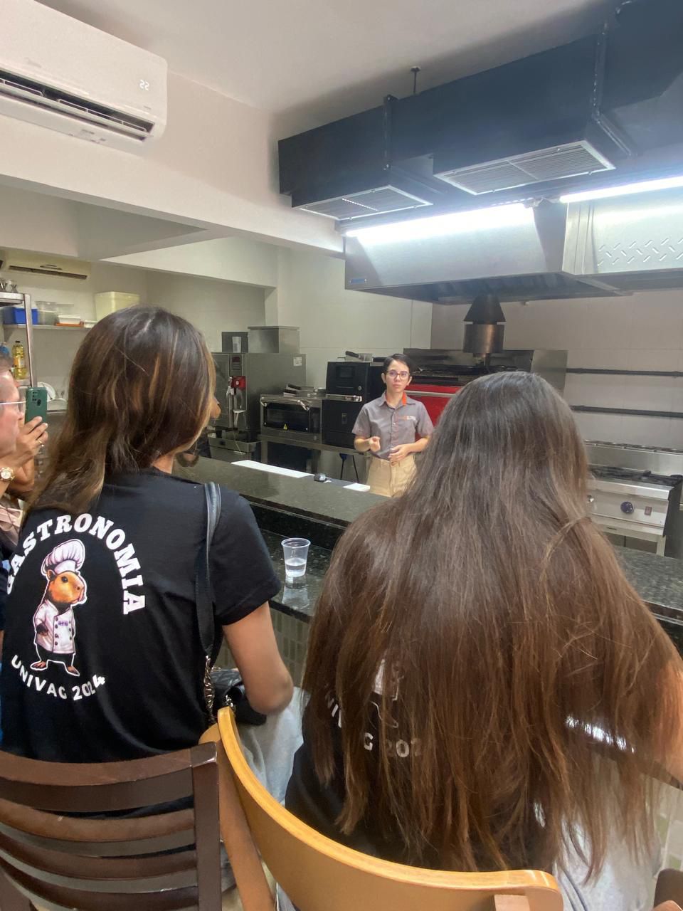Uma mulher vestindo uma camisa preta que diz gastronomia está sentada em uma cadeira