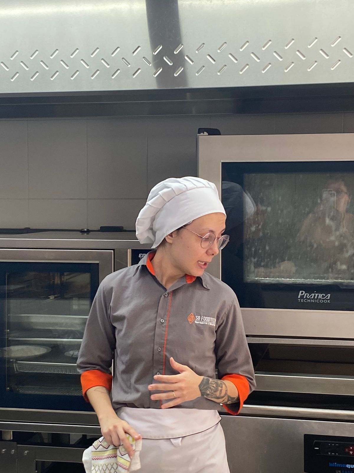 Uma mulher com um chapéu de chef está parada em frente a um forno em uma cozinha.