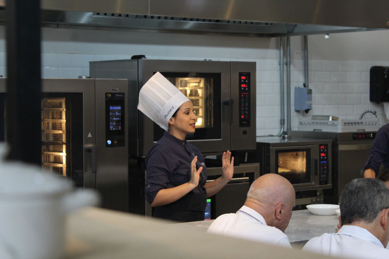 Uma mulher com chapéu de chef está fazendo uma apresentação em uma cozinha