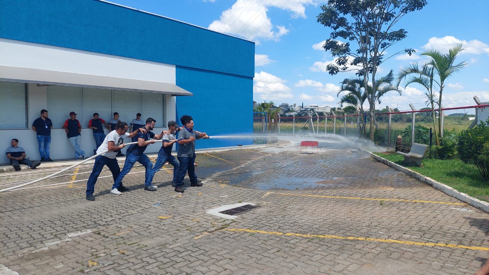 Um grupo de pessoas está puxando uma mangueira em frente a um prédio azul.
