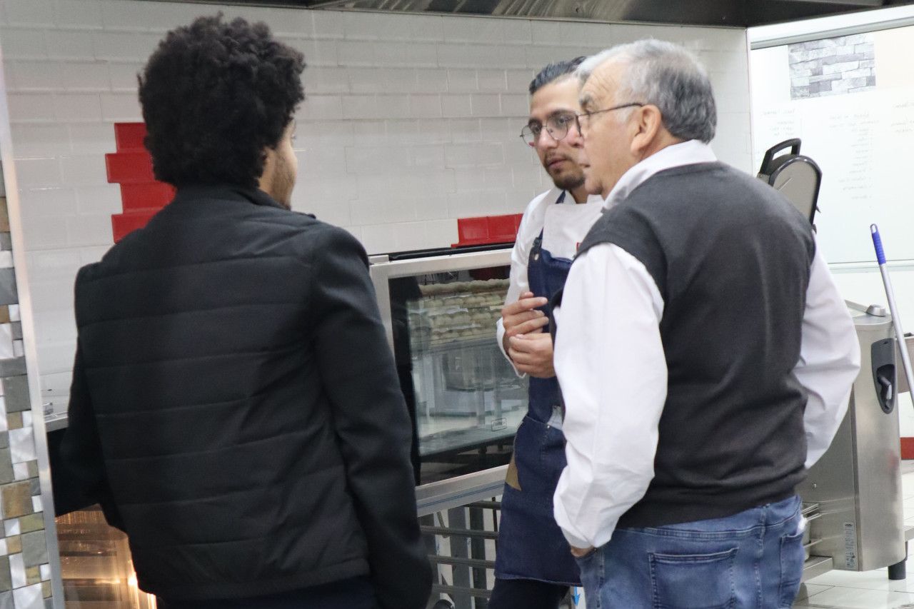 Três homens estão em uma cozinha conversando entre si.