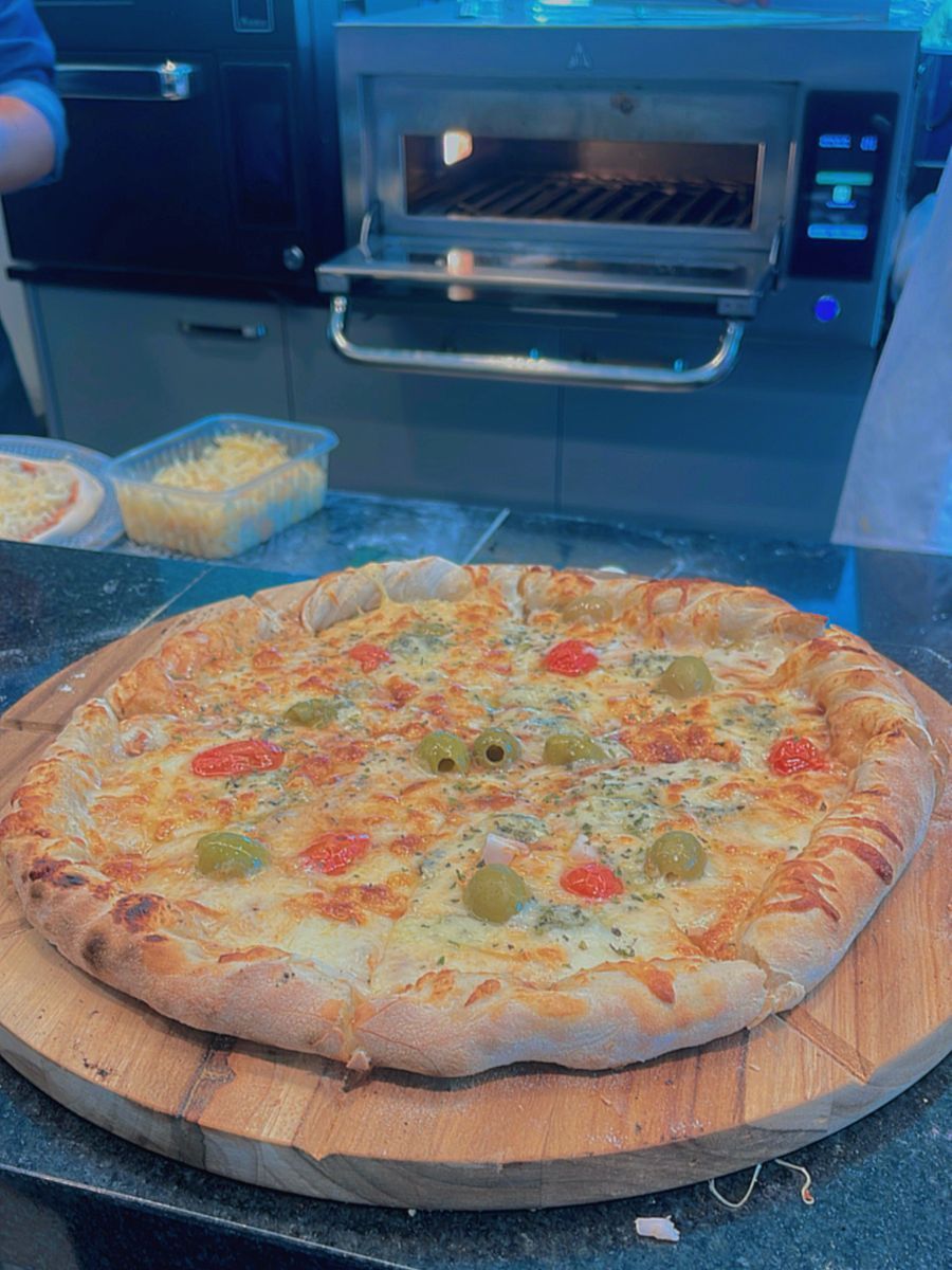 Uma pizza está sobre uma tábua de corte de madeira em uma mesa.