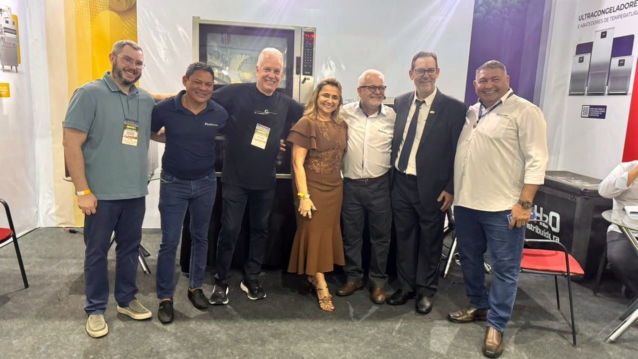 Grupo de sete pessoas posando juntas em um estande de feira, sorrindo para a câmera.