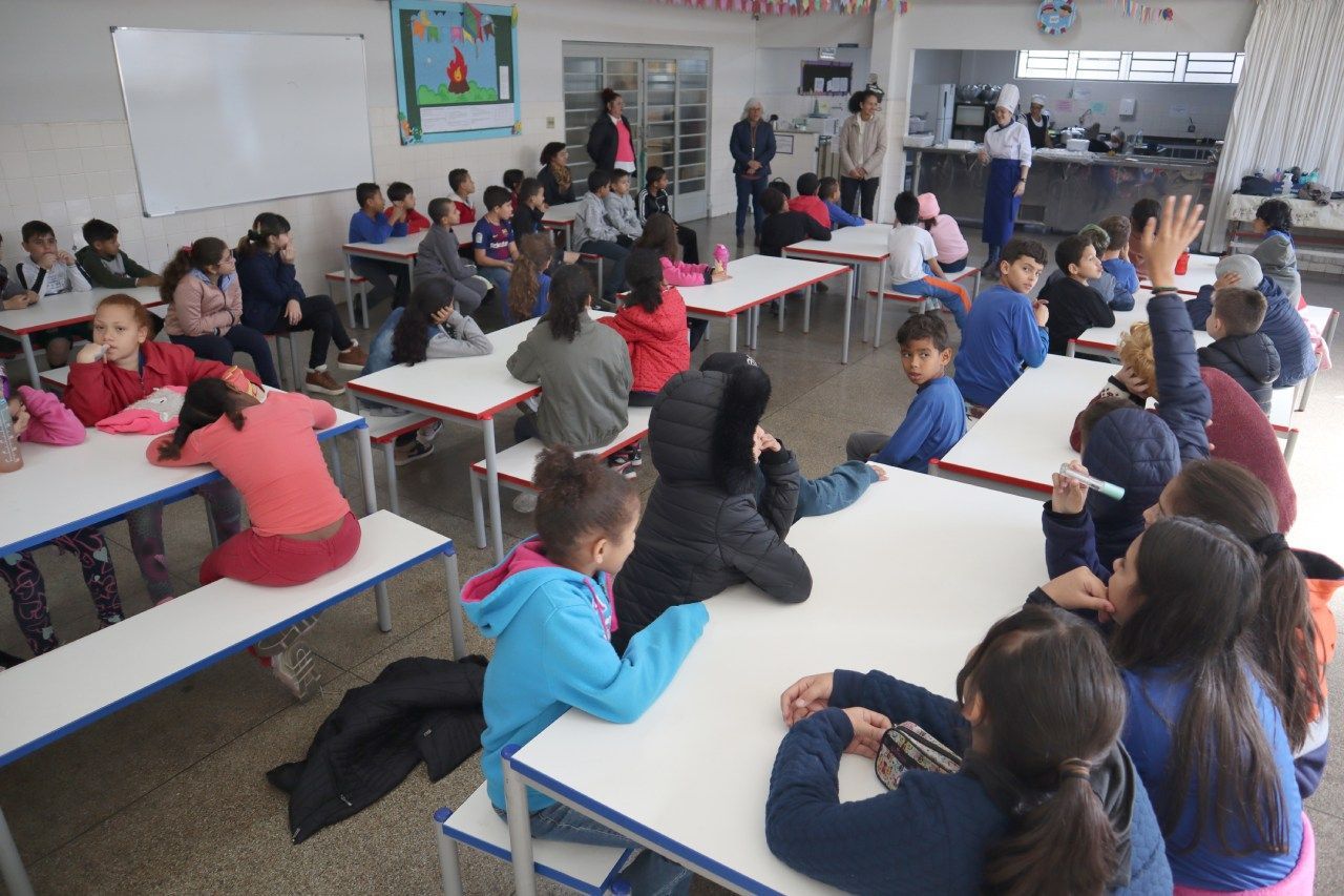 Um grupo de crianças está sentado em mesas em um refeitório escolar