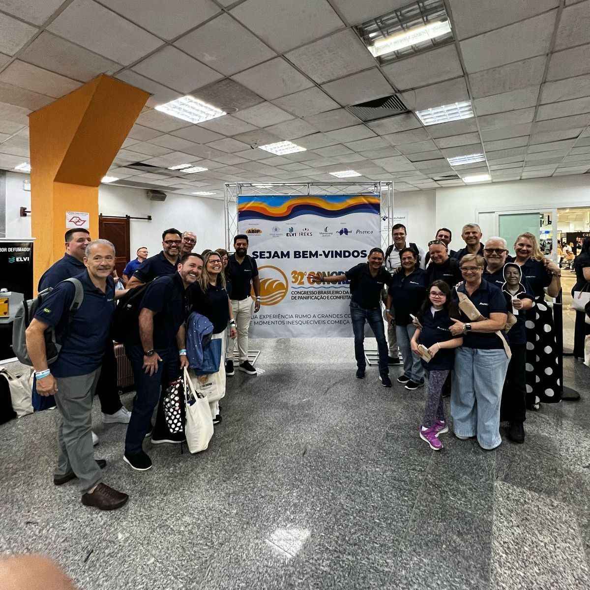 Um grupo de pessoas está posando para uma foto em frente a uma placa que diz 'sonia'