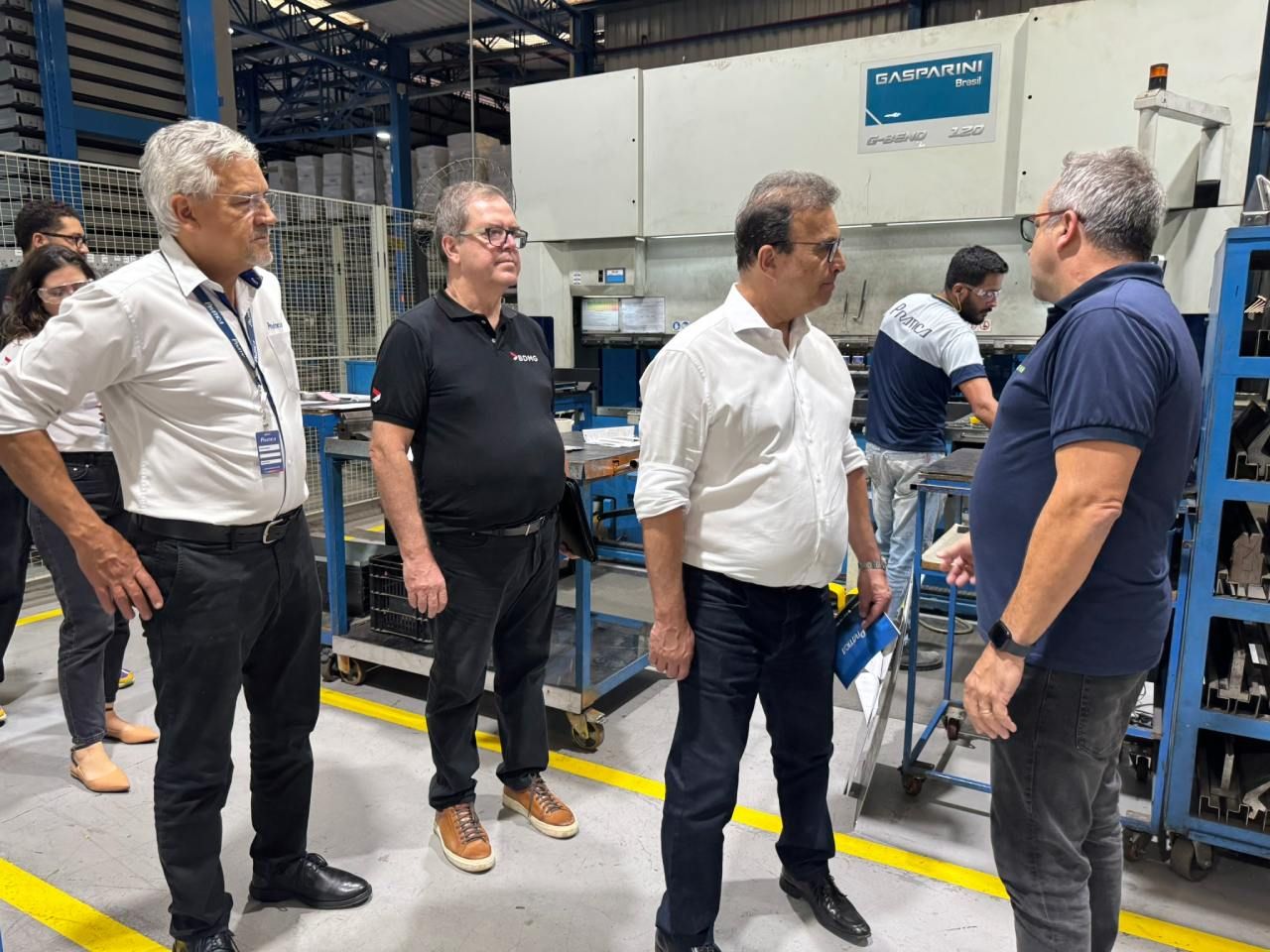 Um grupo de homens está em uma fábrica conversando entre si.