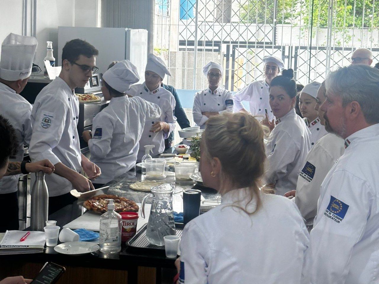 Um grupo de chefs estão em volta de uma mesa em uma cozinha