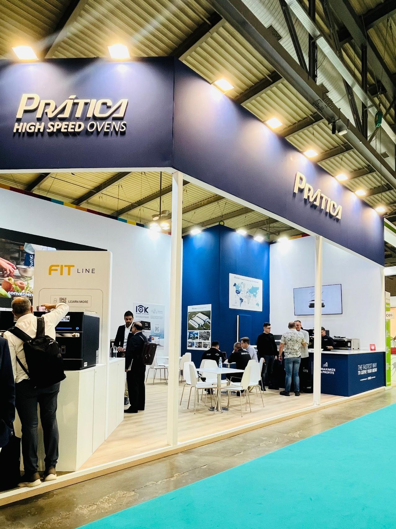 Estande da Prática em uma feira. Pessoas em pé ao lado dos expositores. As cores azul e branco predominam.