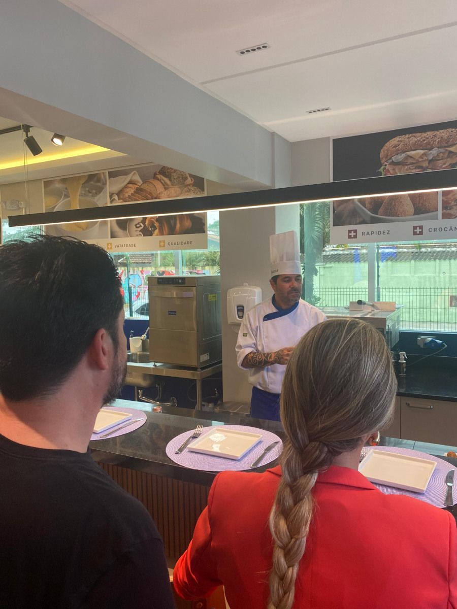 Um homem e uma mulher estão em frente a um chef em um restaurante.