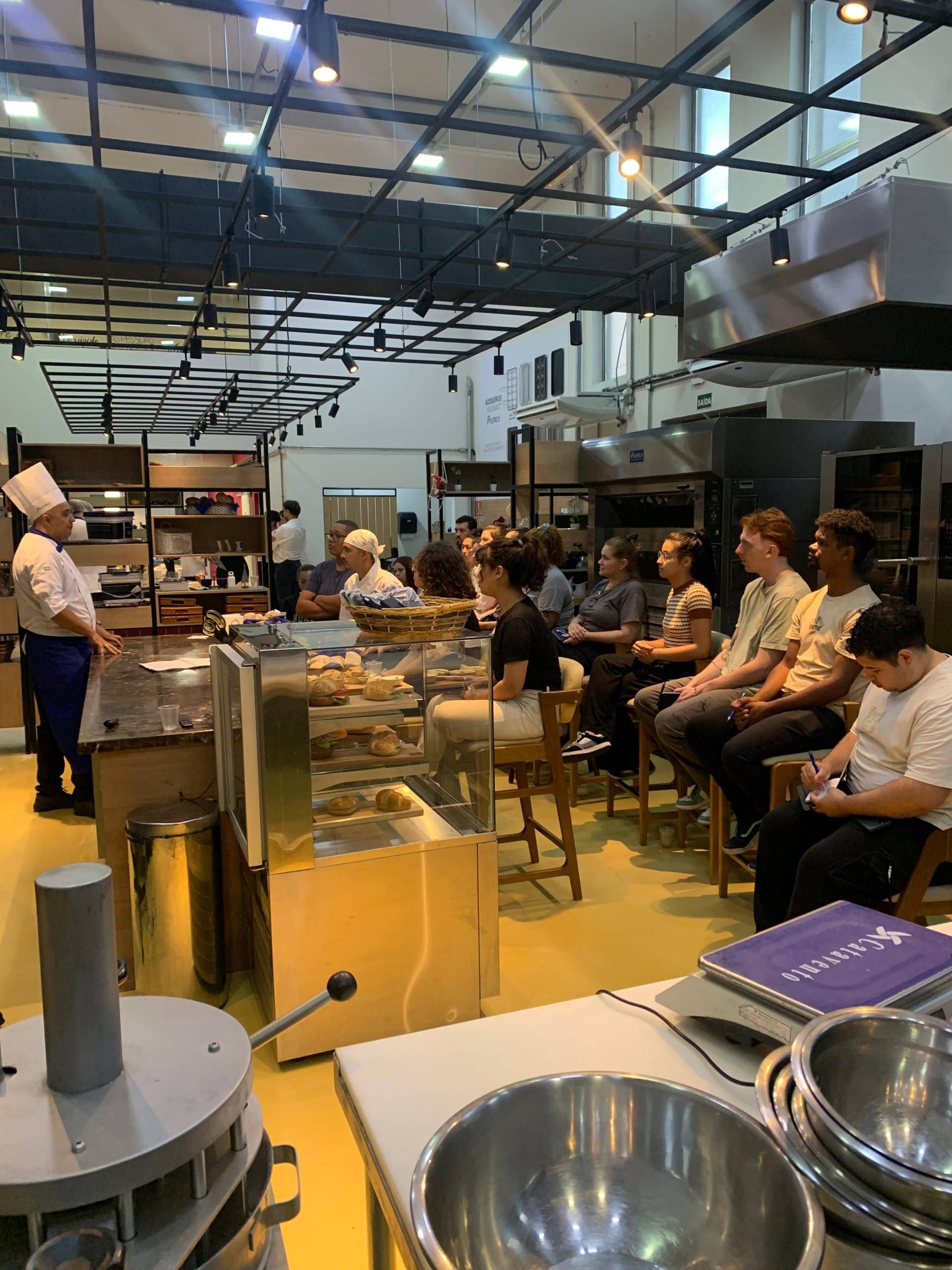 Um grupo de pessoas está sentado em mesas em uma cozinha.