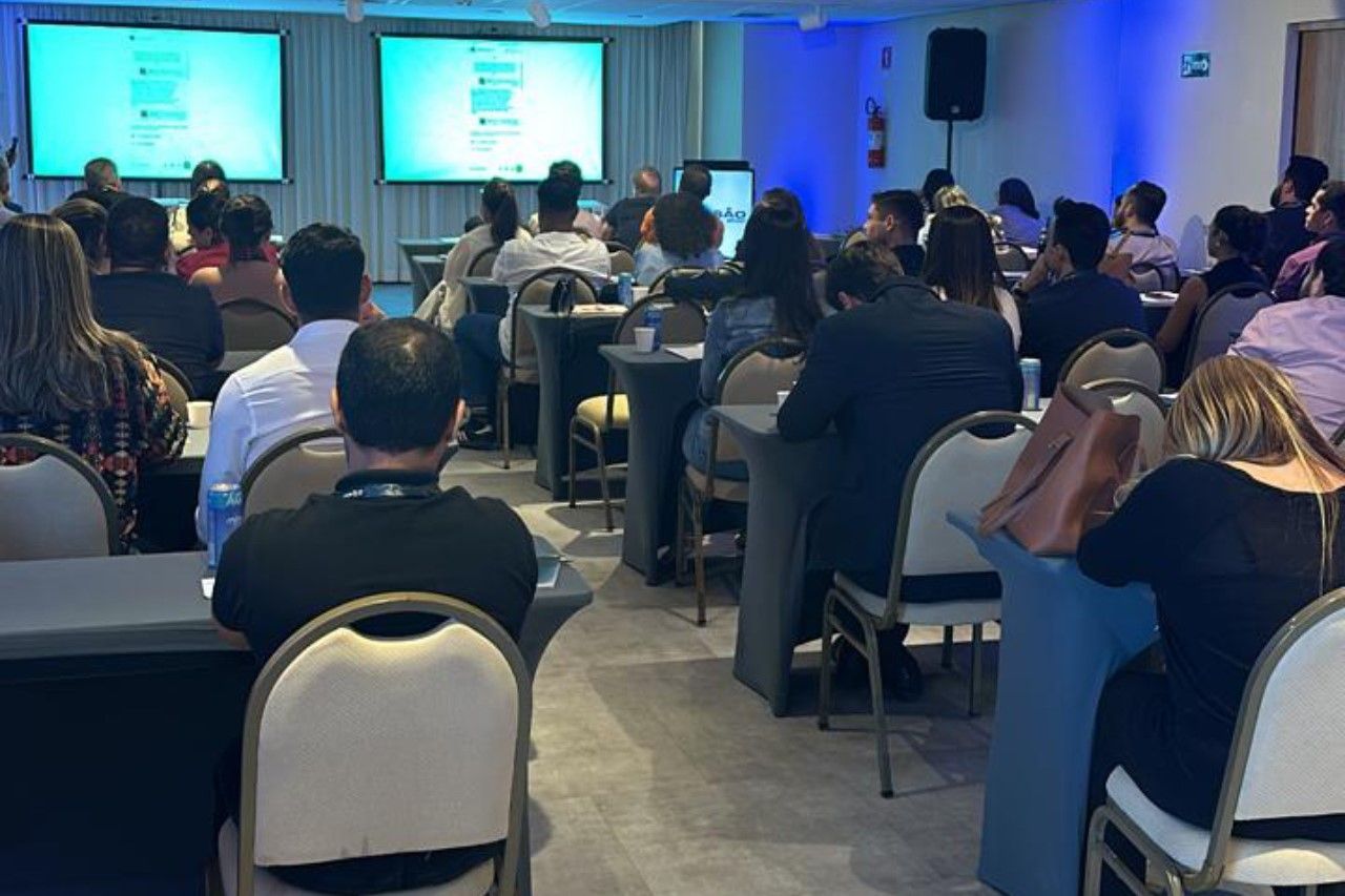 Um grande grupo de pessoas está sentado em mesas em uma sala de conferências.