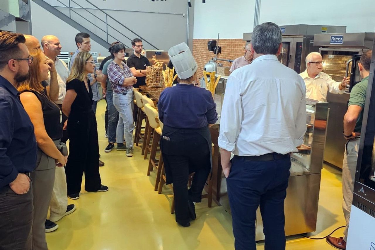 Um grupo de pessoas está em pé ao redor de uma mesa na cozinha.
