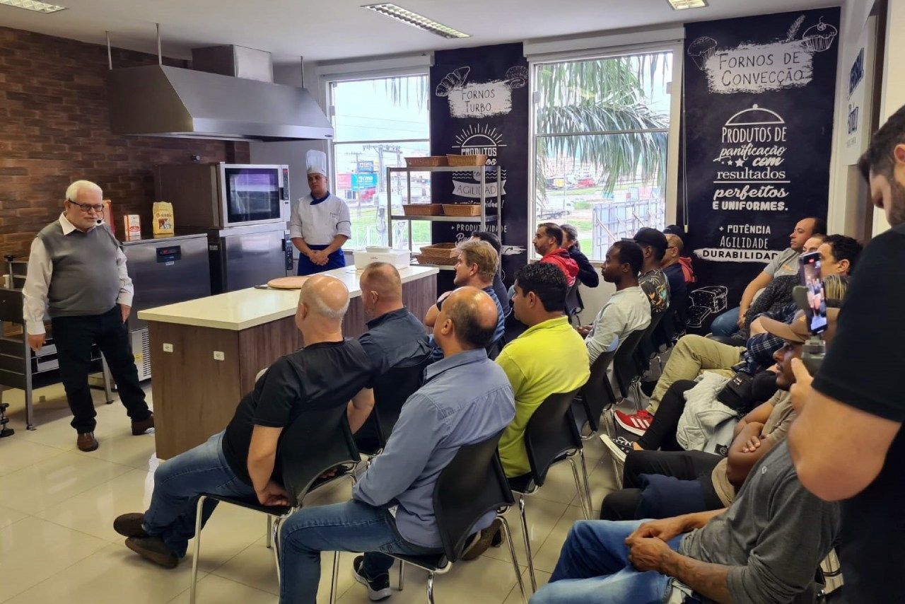 Um grupo de pessoas está sentado em cadeiras em uma sala assistindo a uma apresentação.