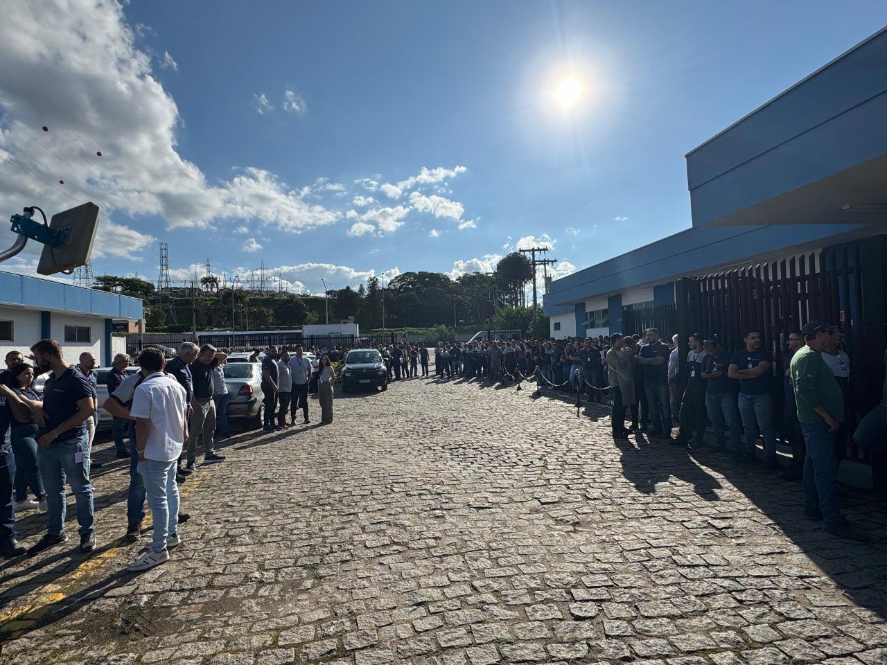 Um grupo de pessoas está parado em uma rua de paralelepípedos em frente a um prédio.