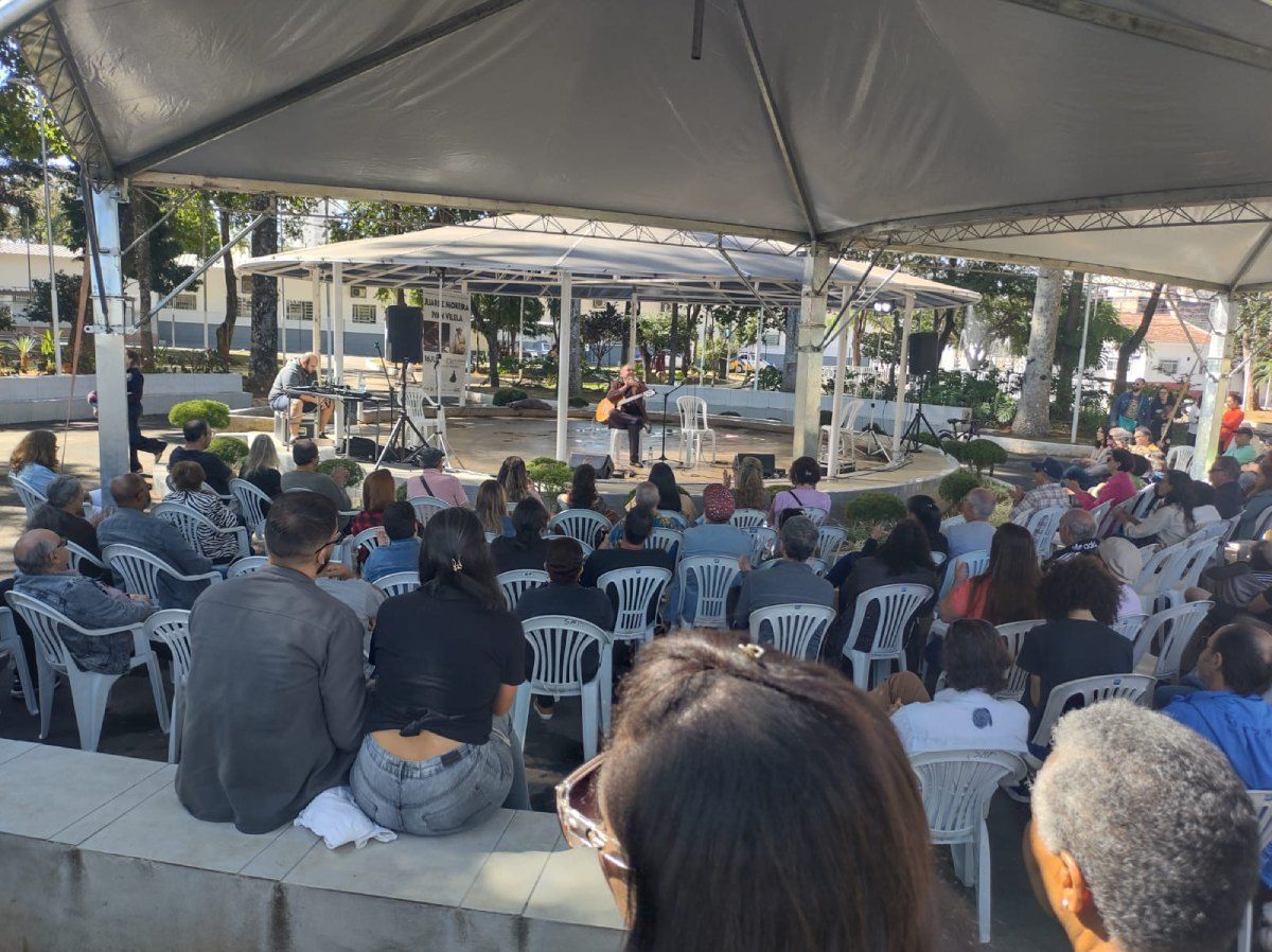 Um grupo de pessoas está sentado sob uma tenda assistindo a um concerto.