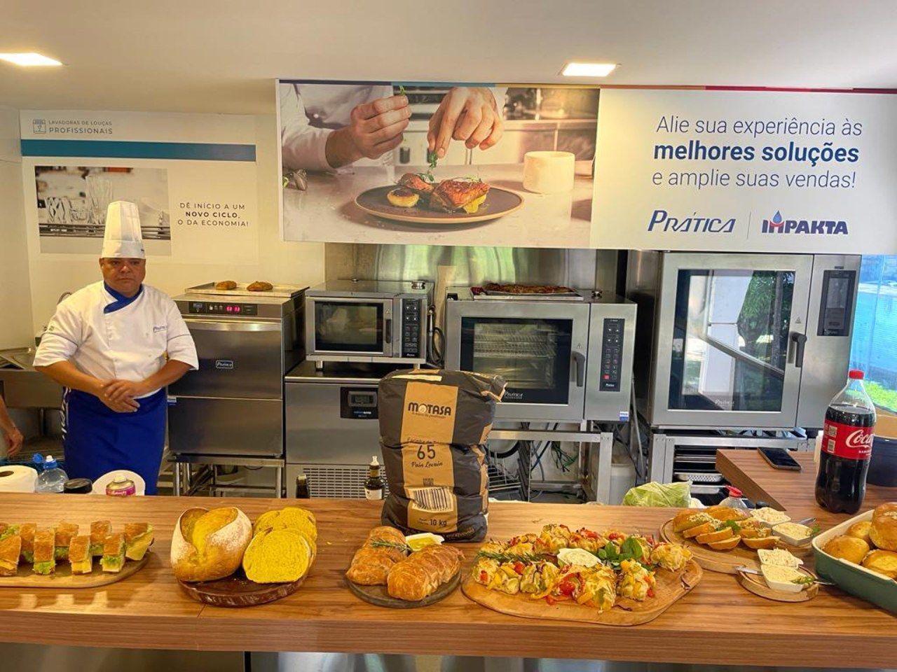 Um homem com chapéu de chef está em uma cozinha rodeado de comida.