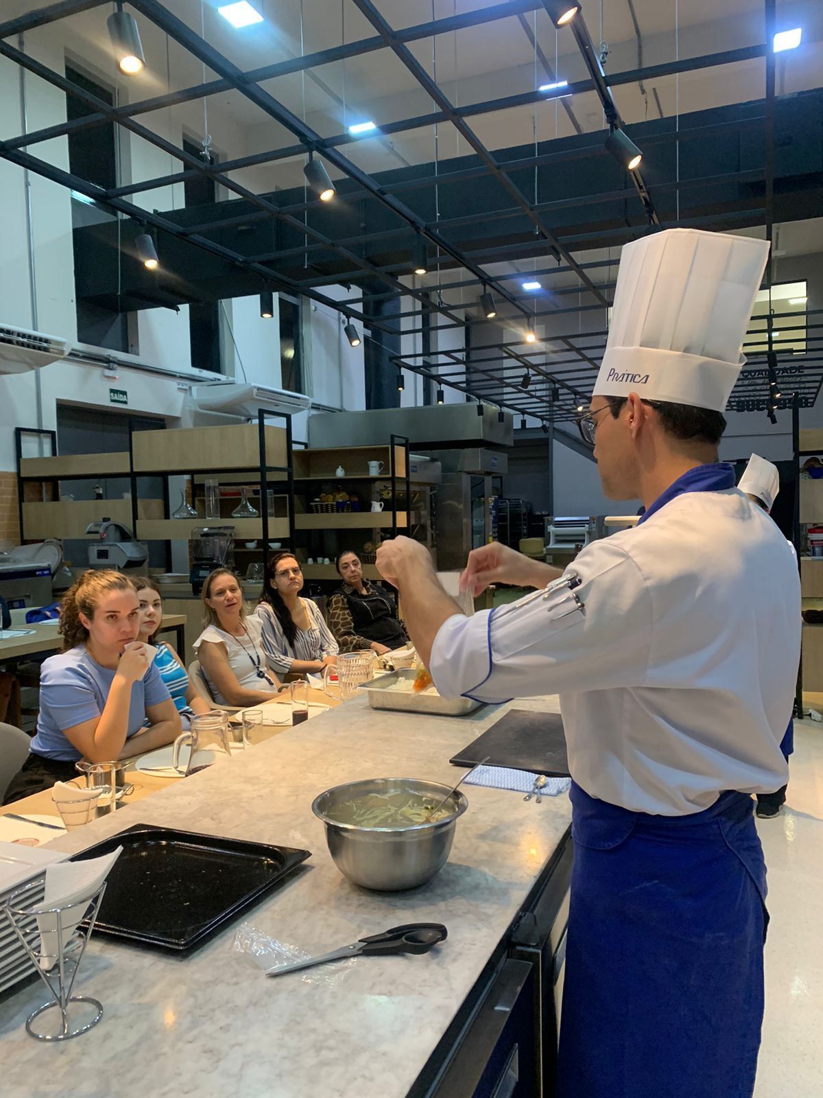 Um chef está ensinando um grupo de pessoas a cozinhar em uma cozinha.