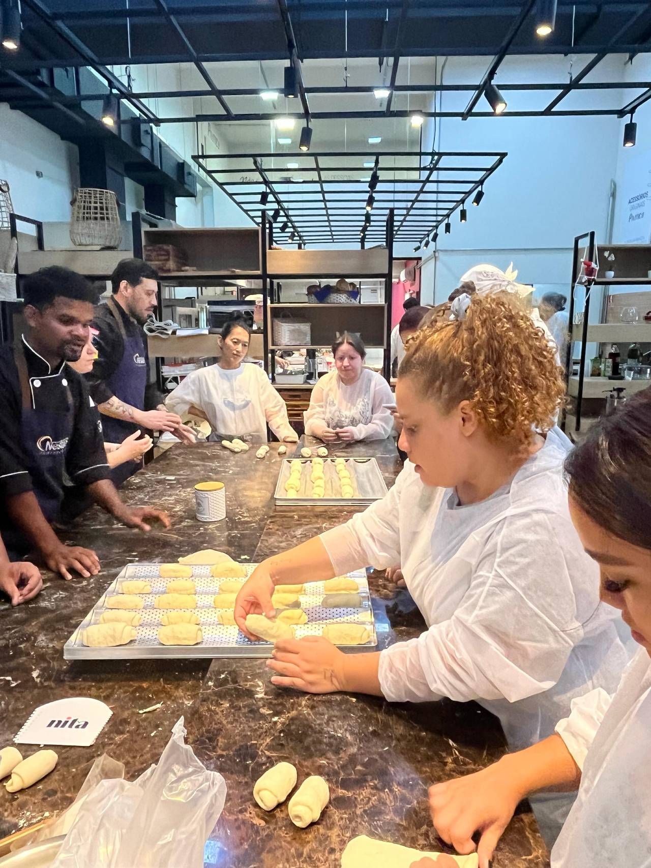 Um grupo de pessoas está sentado à mesa em uma padaria fazendo massa.