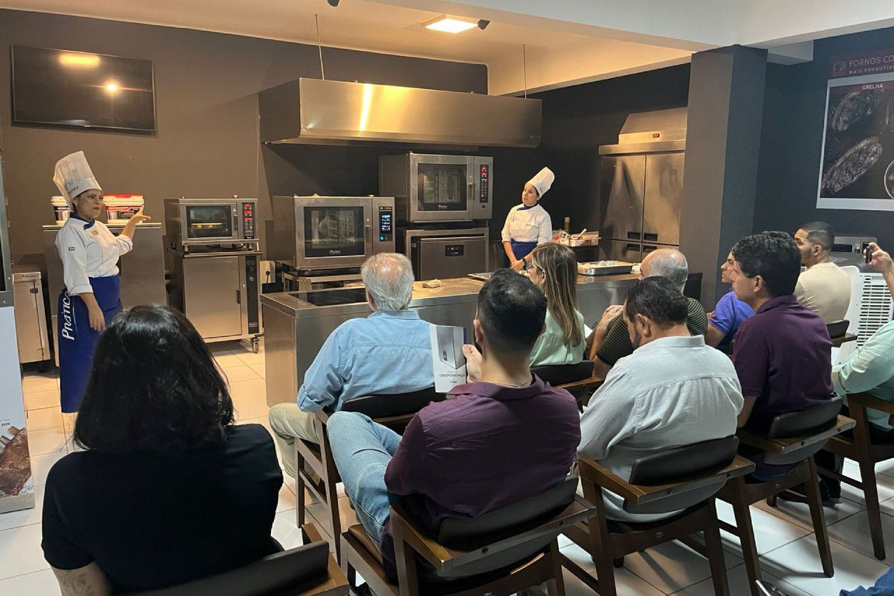 Um grupo de pessoas está sentado em cadeiras em frente a um chef em uma cozinha.